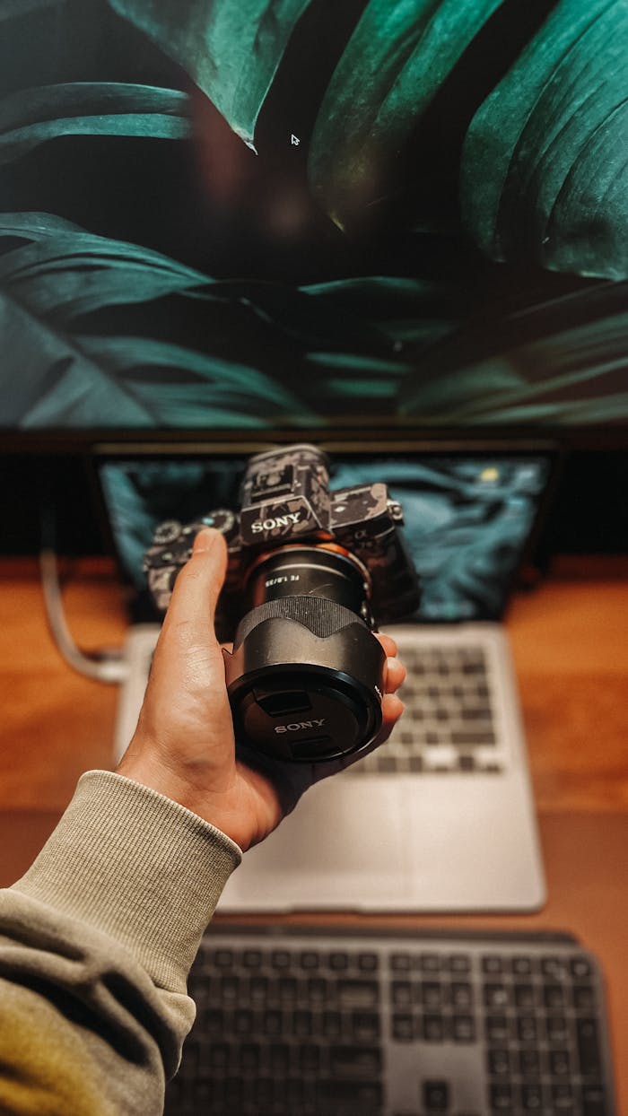 Person holding a camera over a laptop, showcasing modern technology and digital media setup.